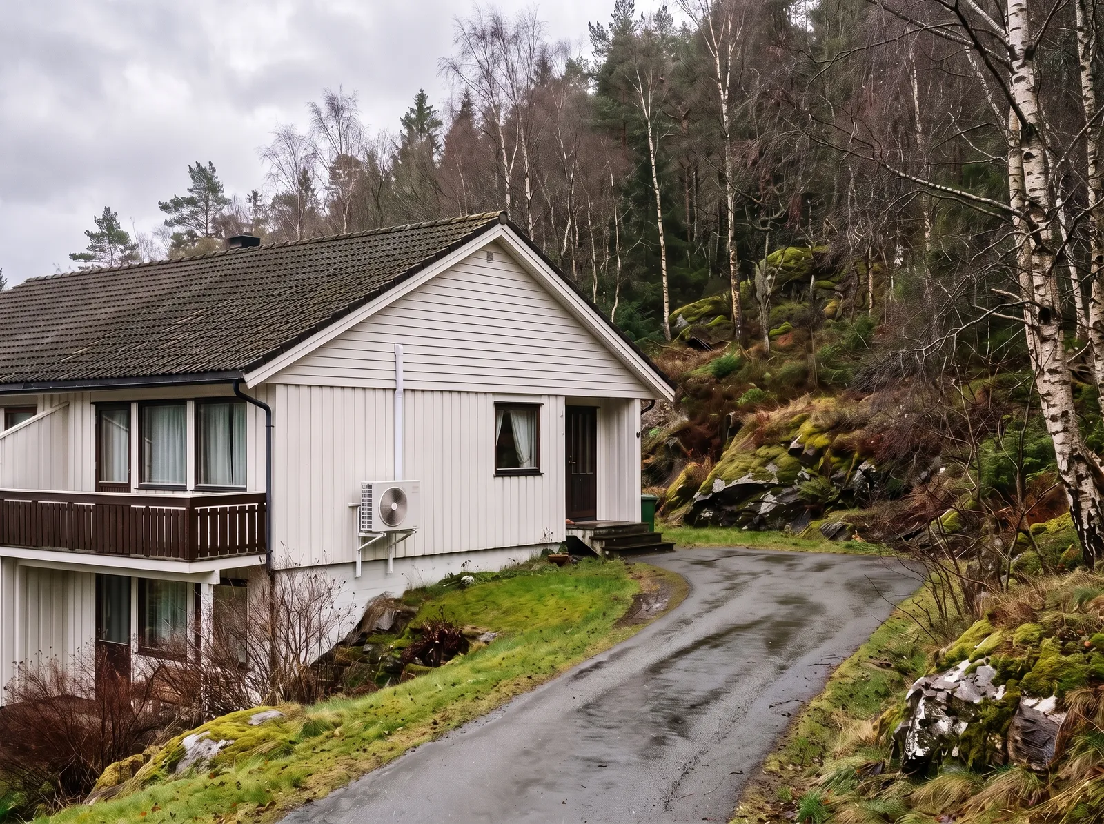 Varmepumpe med utedel på vegg av enebolig i bratt skogsterreng, typisk for Åsane